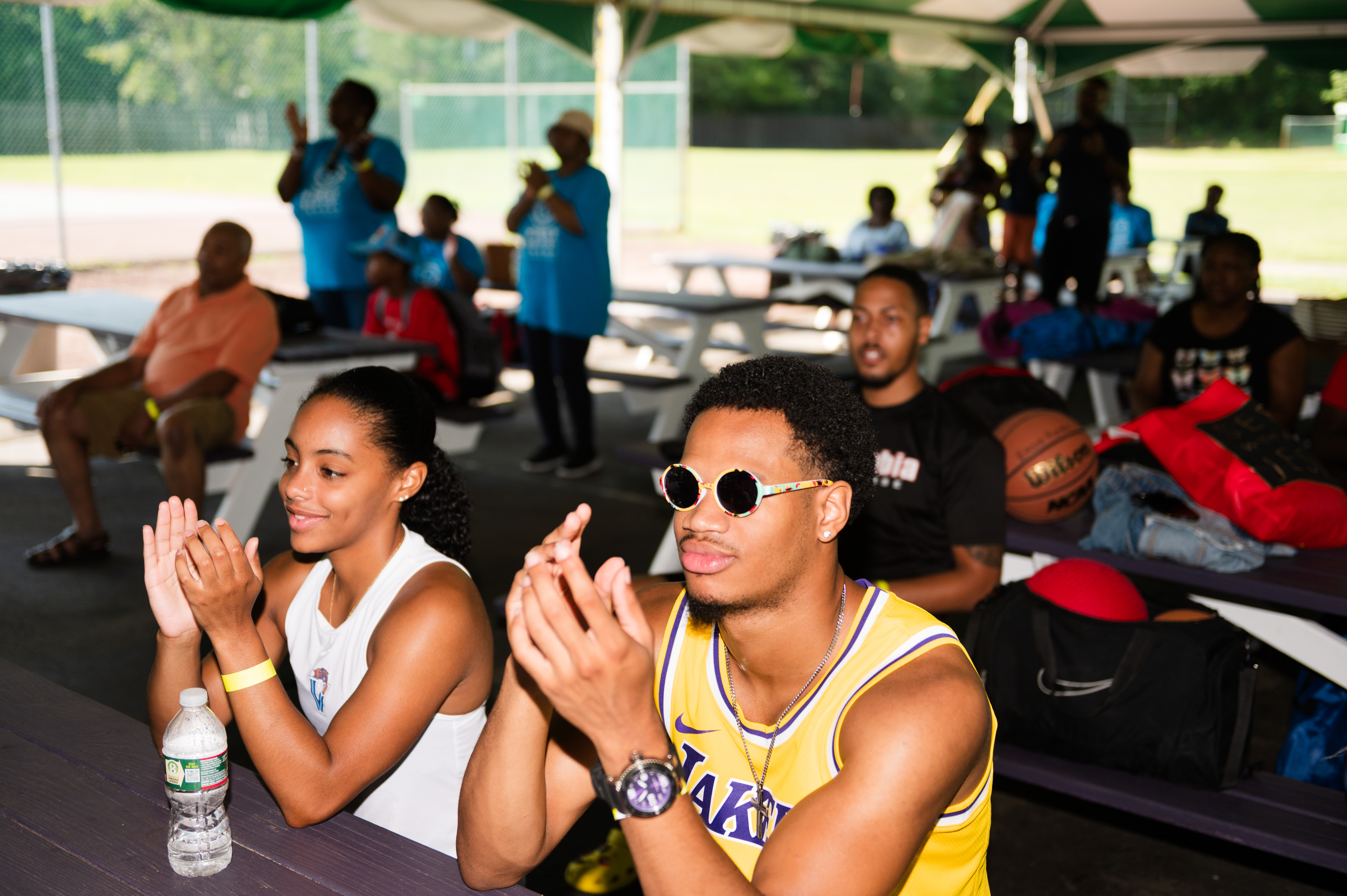 man and woman in tank tops seated at table under tent and clapping