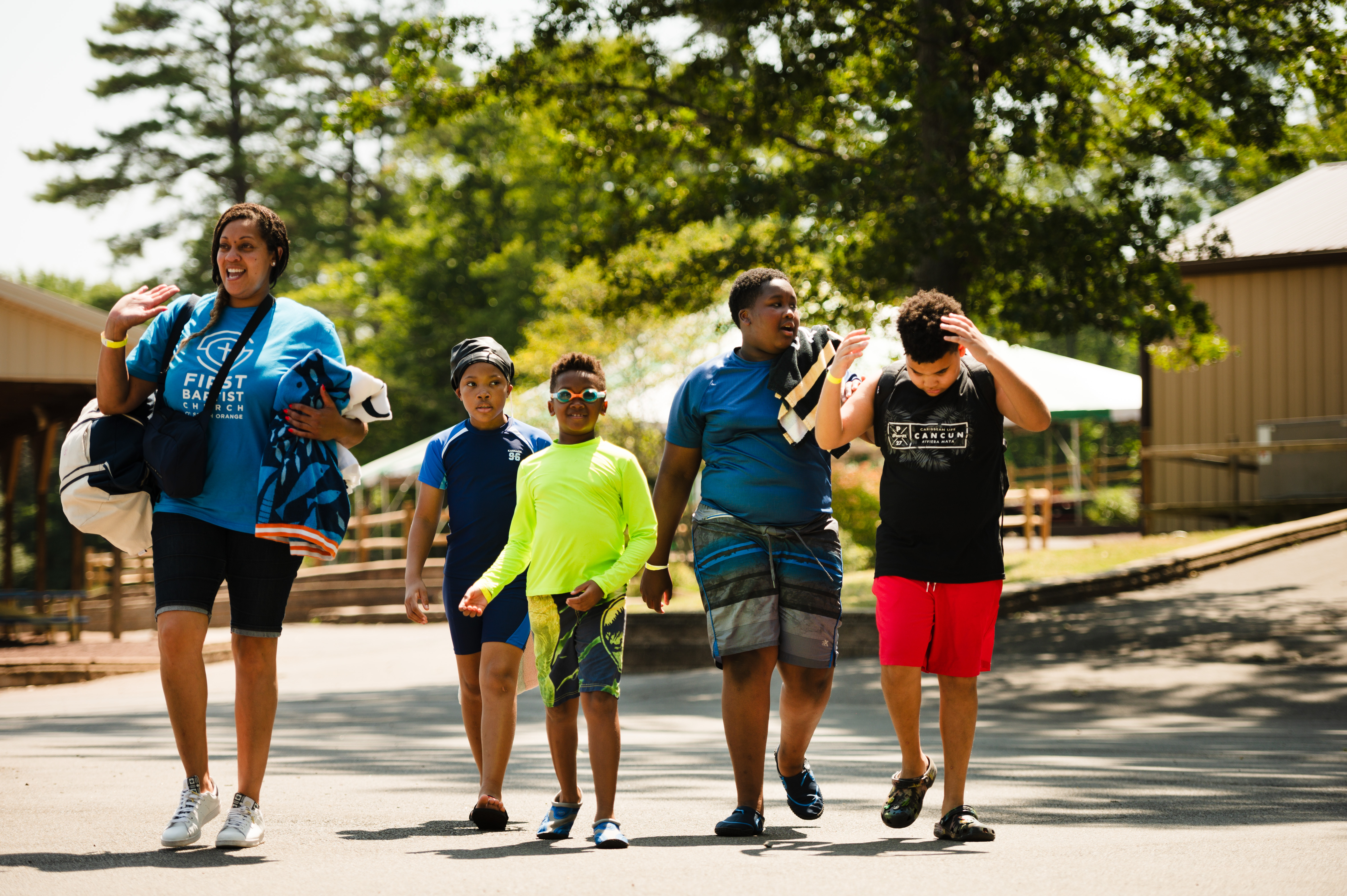 woman walking outdoors with group of kids in swimsuits